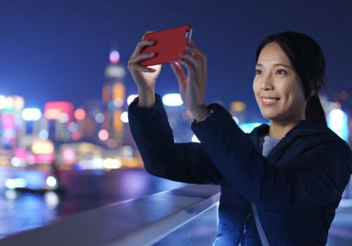 Foto de una mujer tomando una fotografía al cielo con un fondo de una ciudad alumbrada