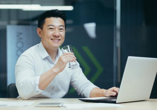 Foto de una persona asiática tomando agua con un computador en su mano