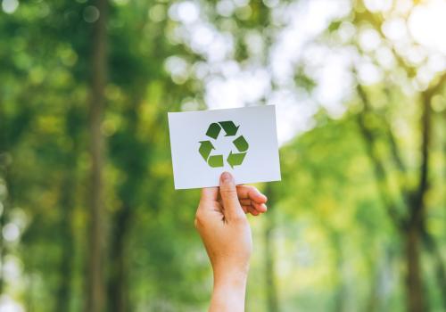 Foto de una persona mostrando con una mano el símbolo de reciclaje con un fondo verde