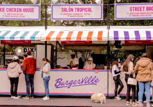 Foto de varias personas haciendo fila frente a unos locales de colores pastel