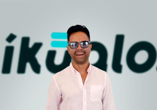 Fotografía de un hombre sonriendo con unas gafas y de fondo el nombre de Ikualo