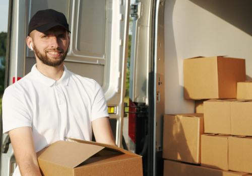 Foto de un un hombre con camiseta blanca y gorra negra alzando una caja sonriendo a la cámara