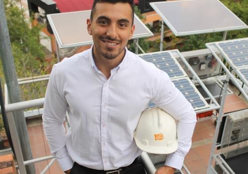 Foto de una persona con un casco posando frente a la cámara con unos paneles solares de fondo