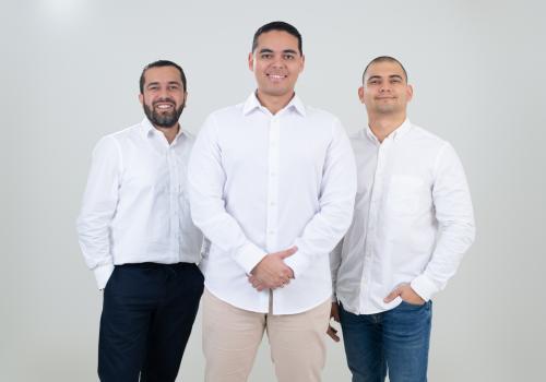 Fotografía de tres hombres con camiseta blanca mirando a la cámara