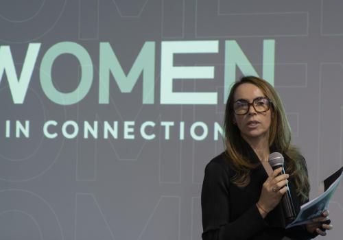 Mujer hablando en un escenario profesional con un fondo que dice Women