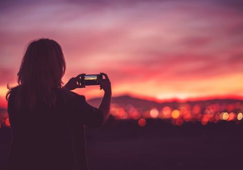 Una mujer tomando una foto sobre un cielo rosado y naranja