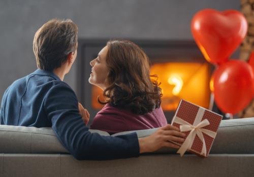 Foto de un hombre y una mujer sentados en un sofa mirando a la chimenea, están abrazados