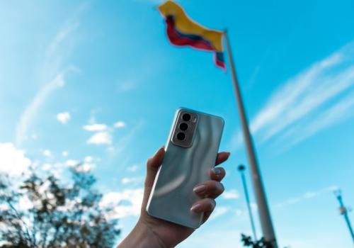 foto de una mano sosteniendo un celular con una bandera de fondo