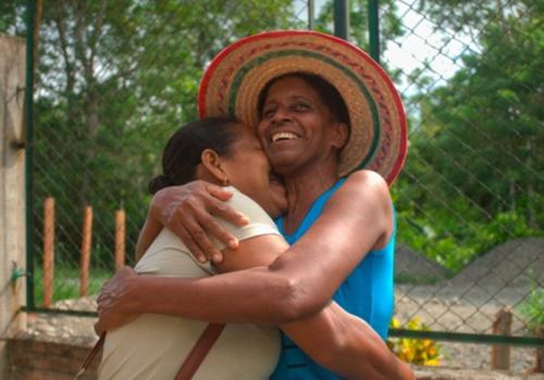 Mujeres abrazandose, una de ellas tiene un sombrero colorido