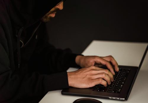 un hombre con capucha negra escribiendo en su laptop