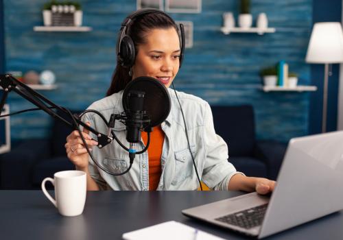 Foto de mujer hablando por micrófono al frente de un computador