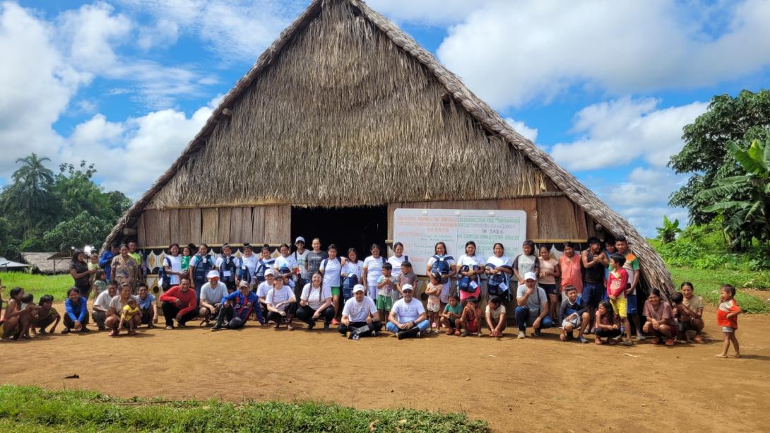 Foto de una casa en paja con 30 personas al frente de ella posando para una fotografía