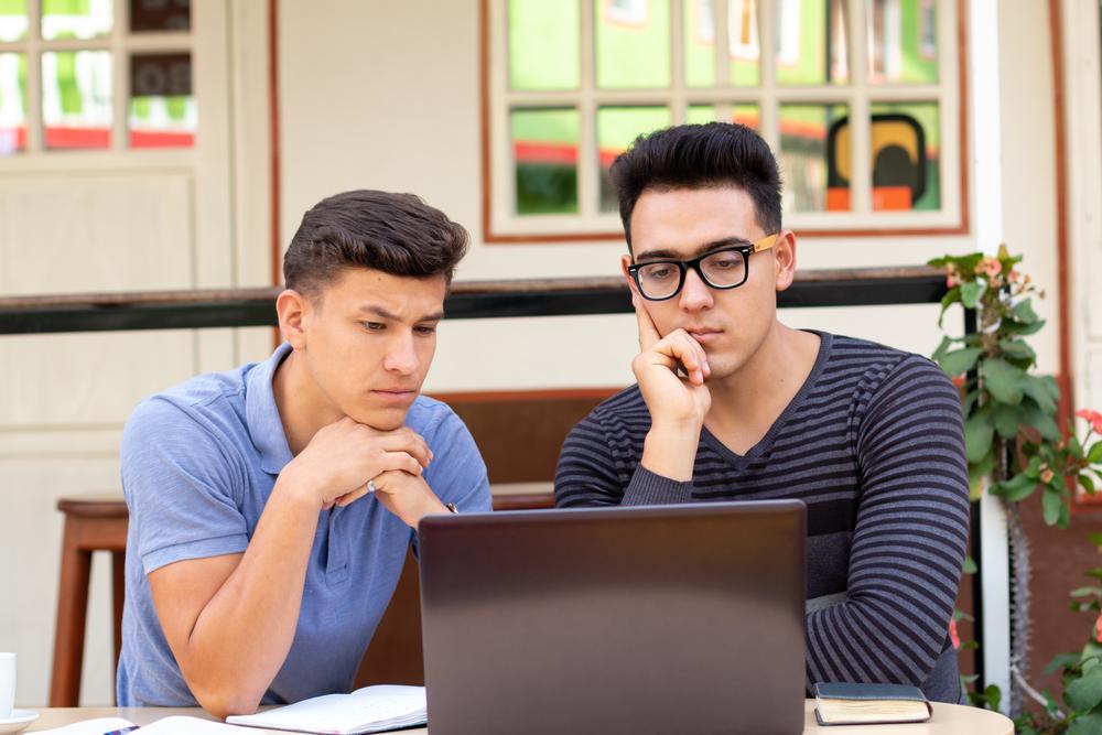 Foto de dos jóvenes mirando el computador mientras piensan