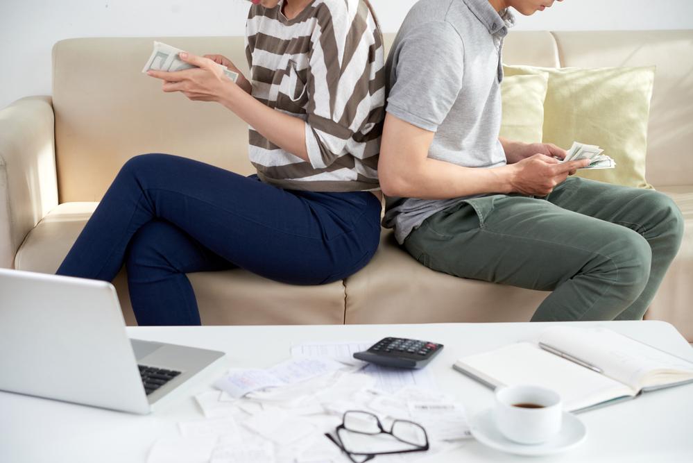 Foto de dos personas de espaldas contanto dinero sobre un sofa