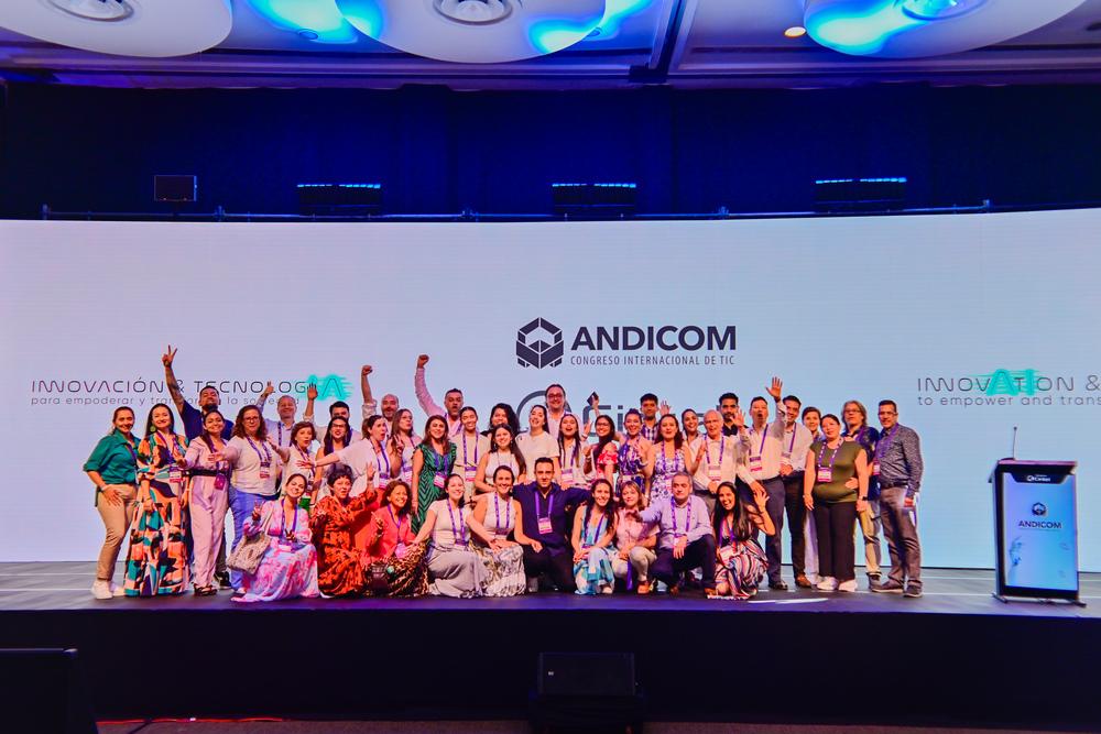 Foto de más de 10 personas reunidas frente a la cámara y un fondo de Andicom en el fondo