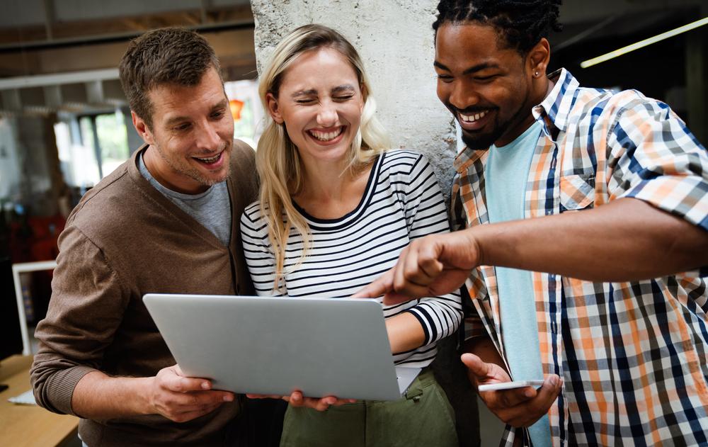 Foto de tres personas mirando un computador y sonriendo a la cámara