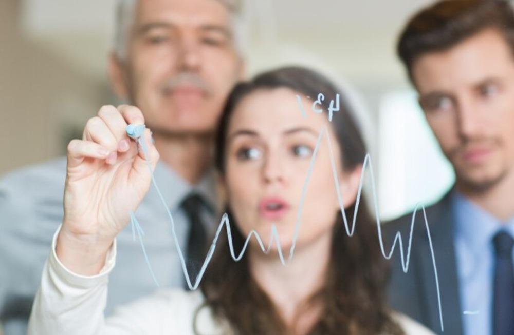 Foto de tres personas mirando unas gráficas sobre un vidrio