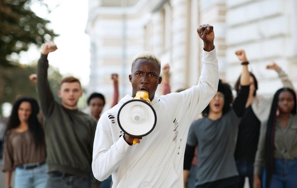 Foto de un hombre afroamericano alzando la mano con un megáfono en mano