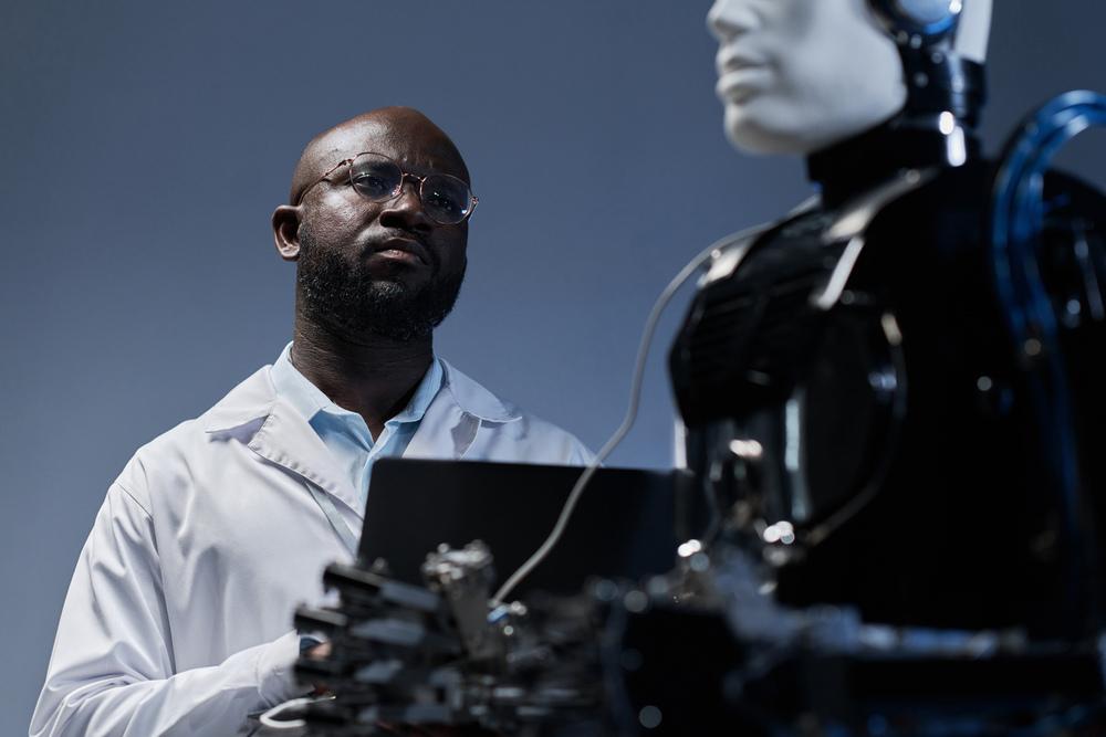 Foto de un hombre americano escribiendo sobre un teclado y mirando un robot