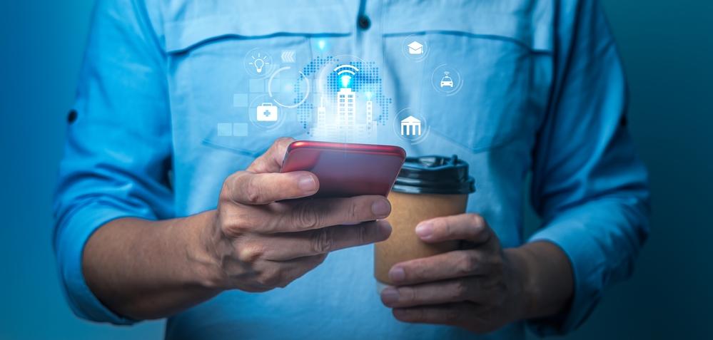 Foto de un hombre utilizando su celular en una mano y con un café en la otra