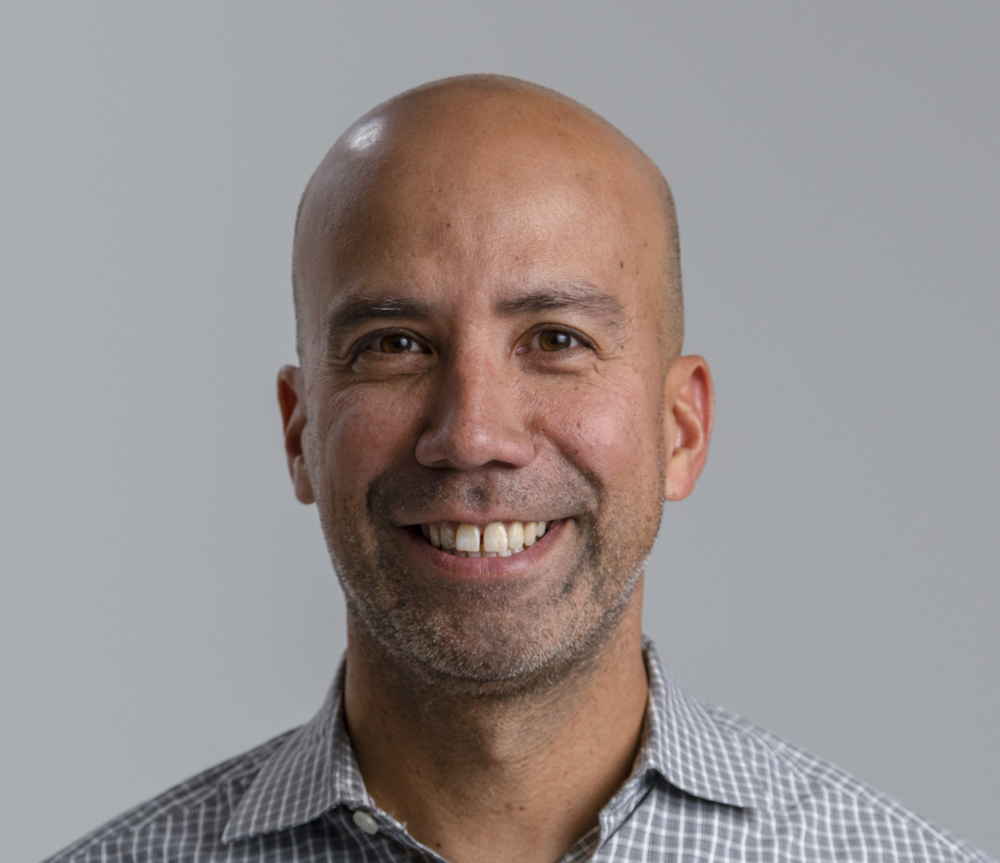 Foto de un hombre sonriente con un fondo gris