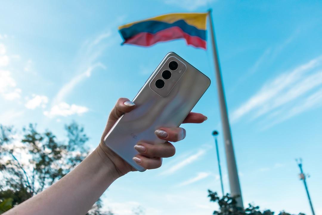 Foto de una mano de mujer con un celular y una bandera de fondo