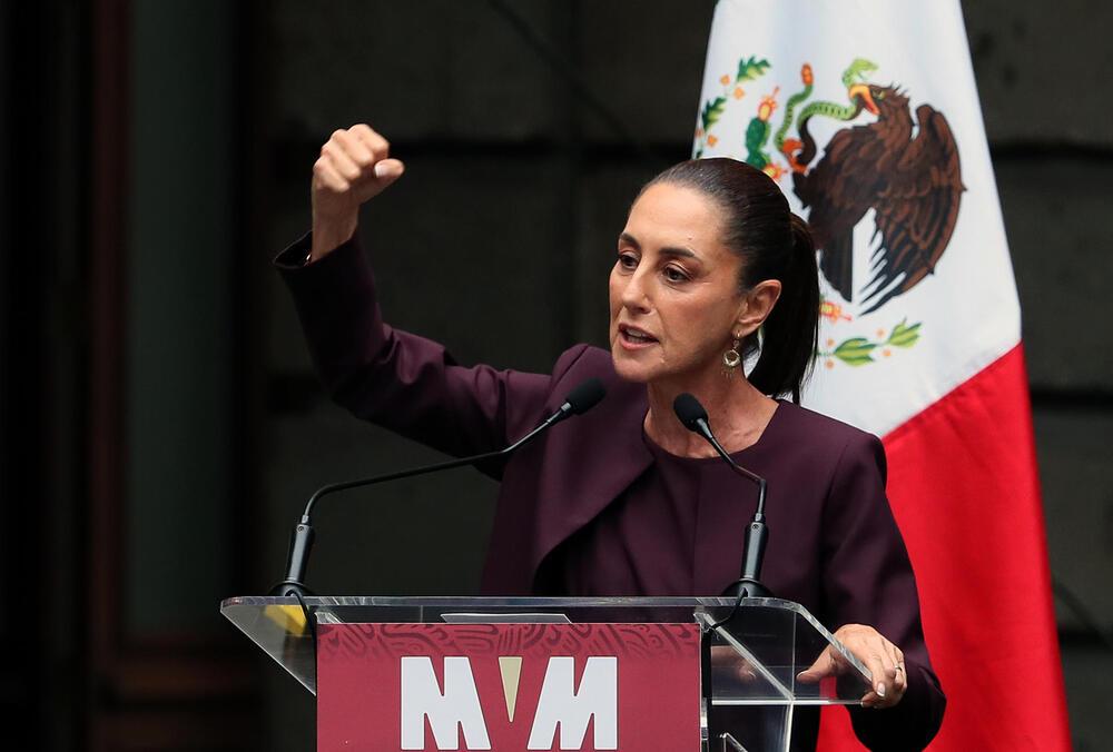 Foto de una mujer con el puño arriba y detrás de ella una bandera de méxico