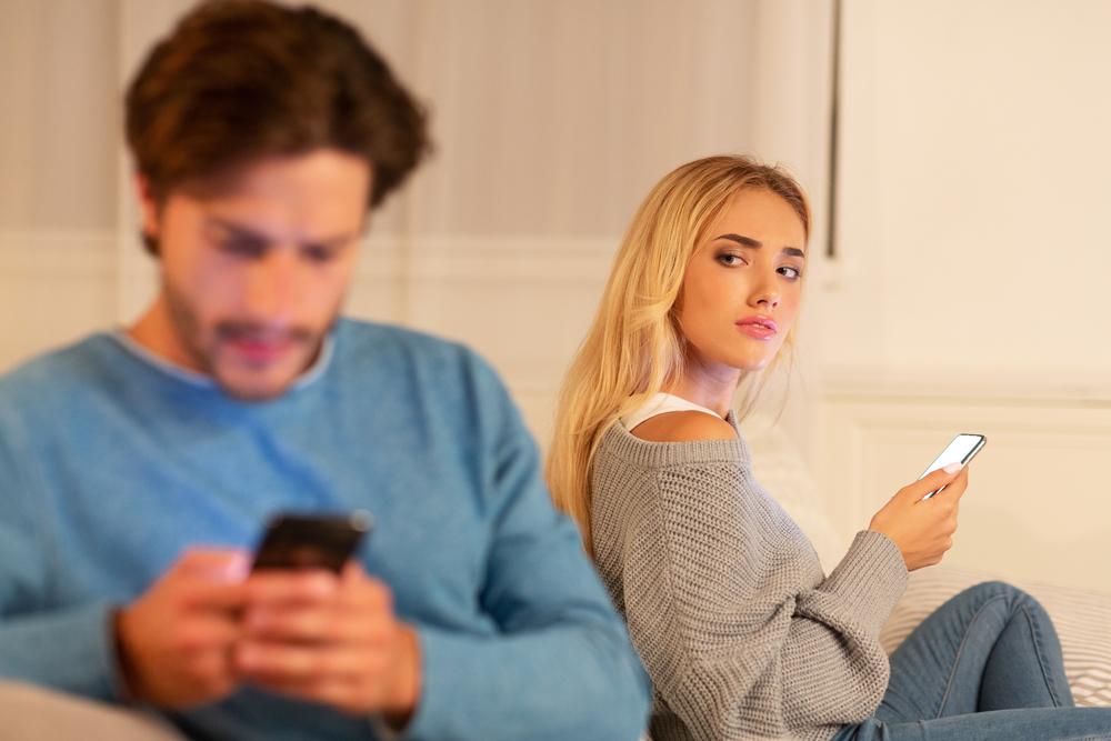 Foto de una mujer con un celular en la mano mirando de forma sospechosa a su pareja que habla por celular