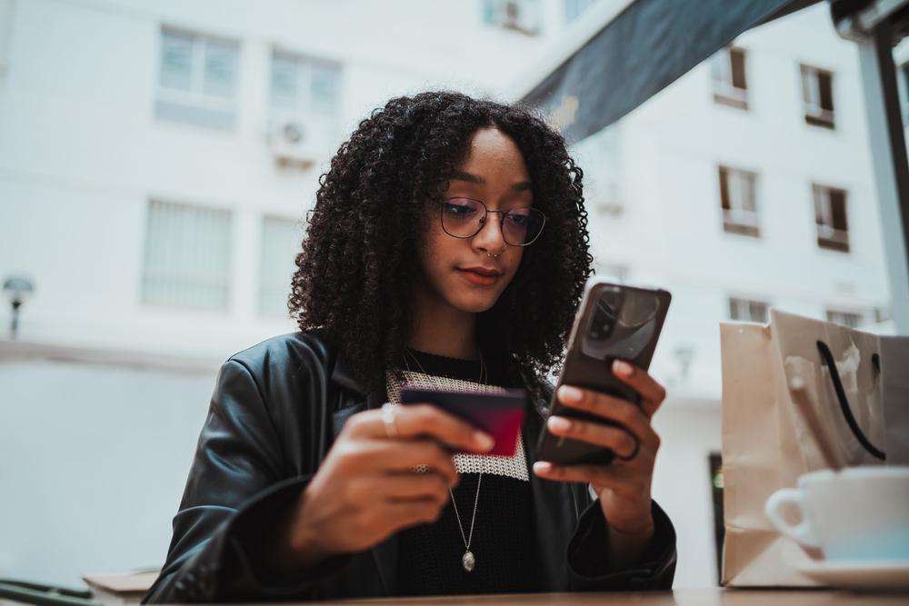 Foto de una mujer con un celular en la mano y una billetera en la otra