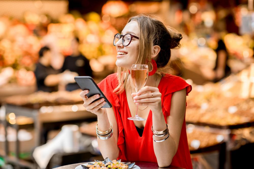 Foto de una mujer con un celular en la mano y una copa en la otra