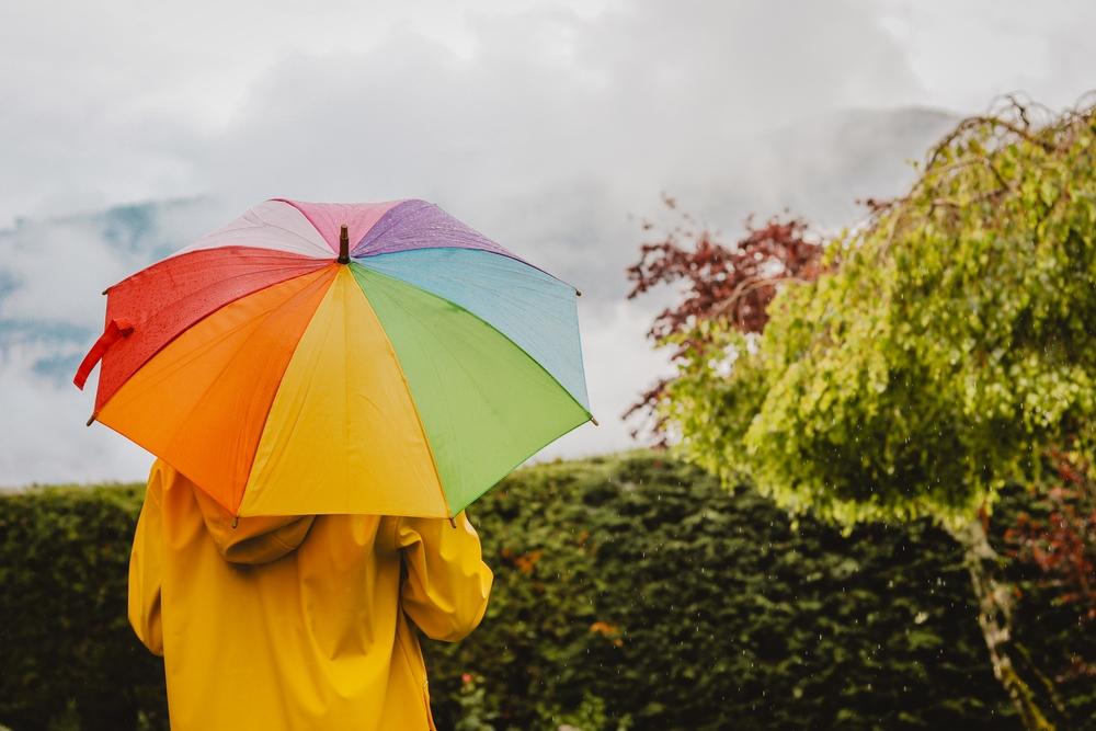 Foto de una mujer con un paraguas abierto de varios colores  de fondo a la cámara