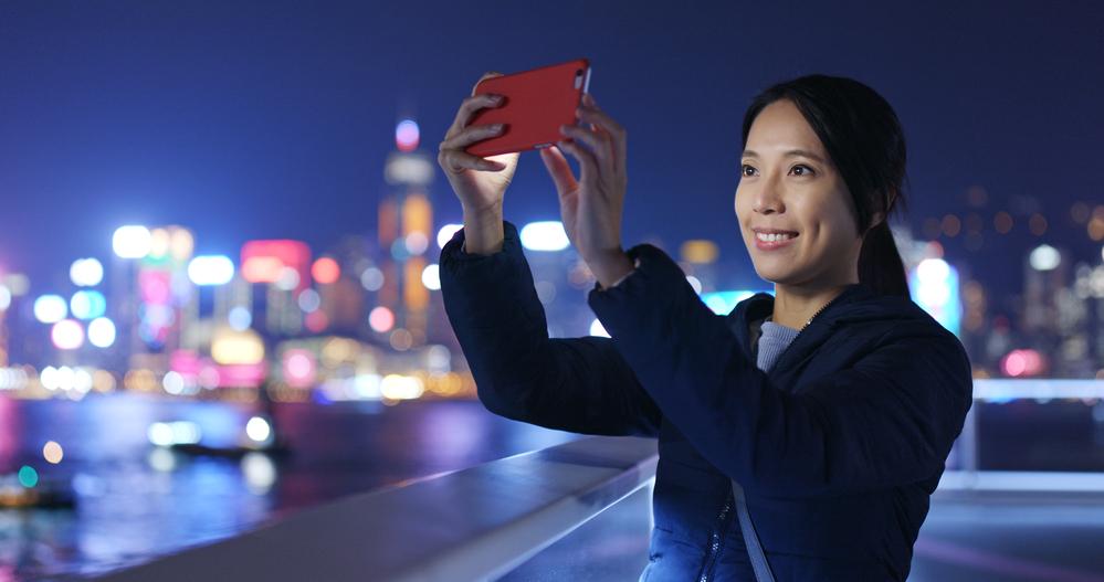 Foto de una mujer tomando una fotografía al cielo con un fondo de una ciudad alumbrada