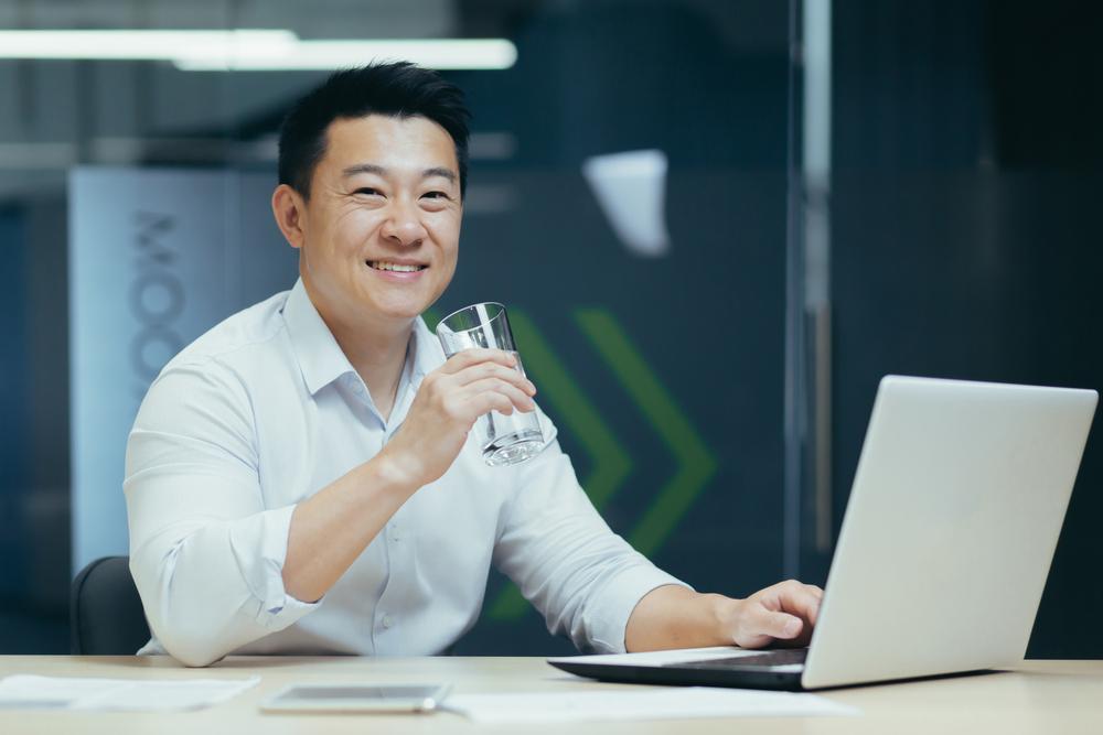 Foto de una persona asiática tomando agua con un computador en su mano