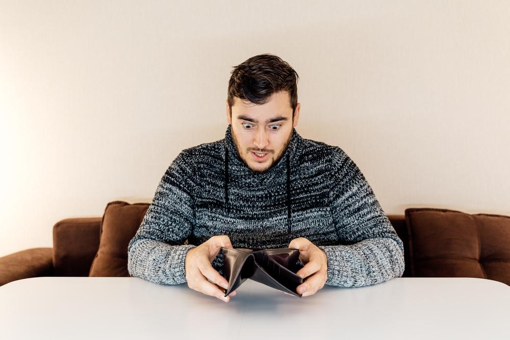 Foto de una persona jóven mirando consternado la billetera