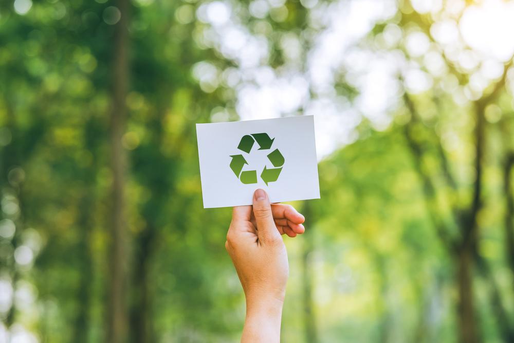 Foto de una persona mostrando con una mano el símbolo de reciclaje con un fondo verde