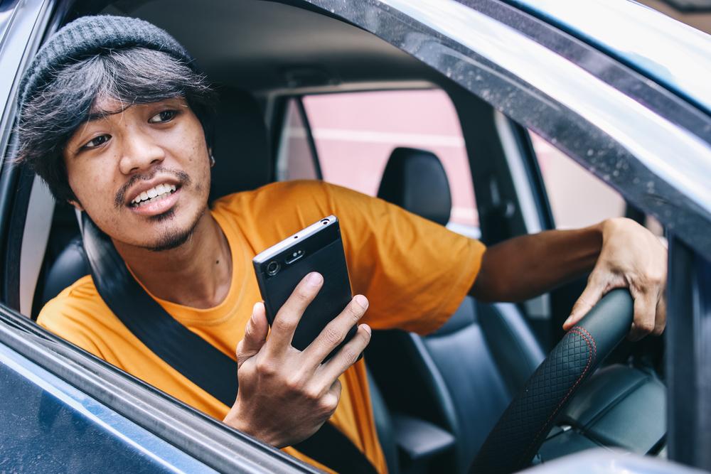 Foto de una persona sacando la cabeza por la ventana con un celular en la mano