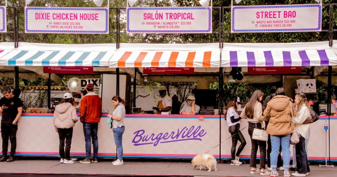 Foto de varias personas haciendo fila frente a unos locales de colores pastel