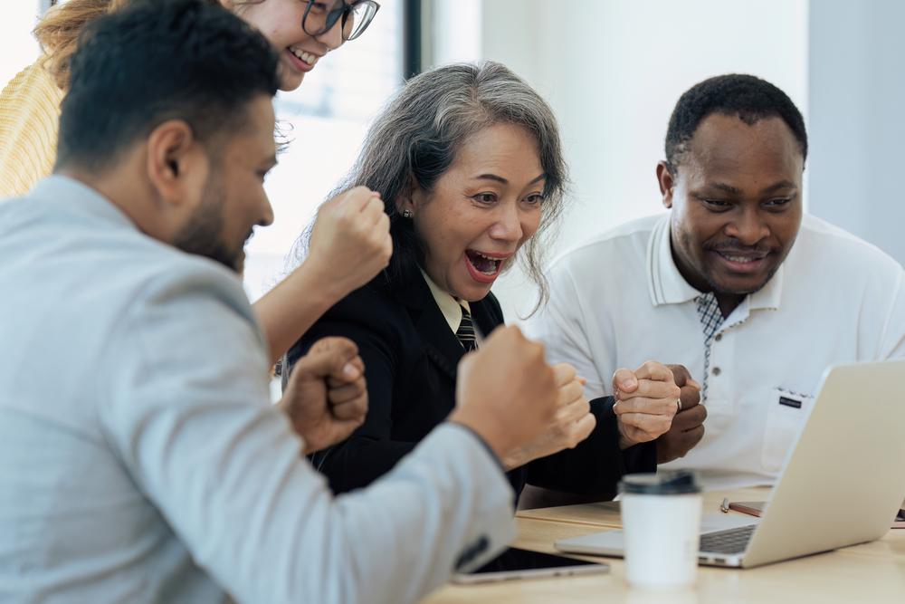 Foto de varias personas reunidas celebrando frente al computador