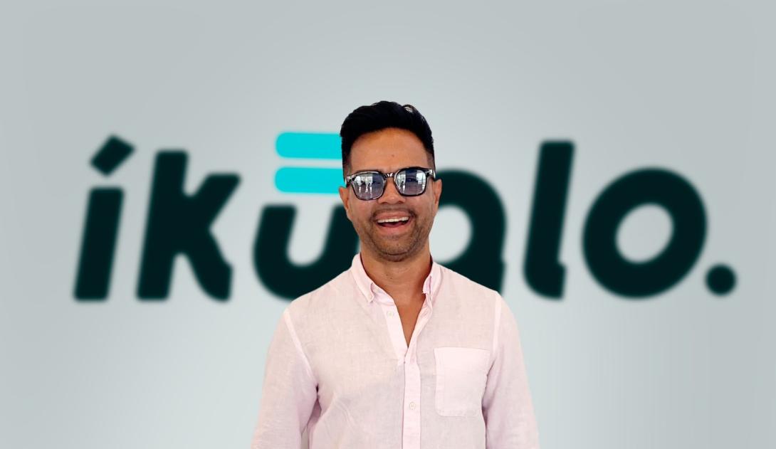 Fotografía de un hombre sonriendo con unas gafas y de fondo el nombre de Ikualo