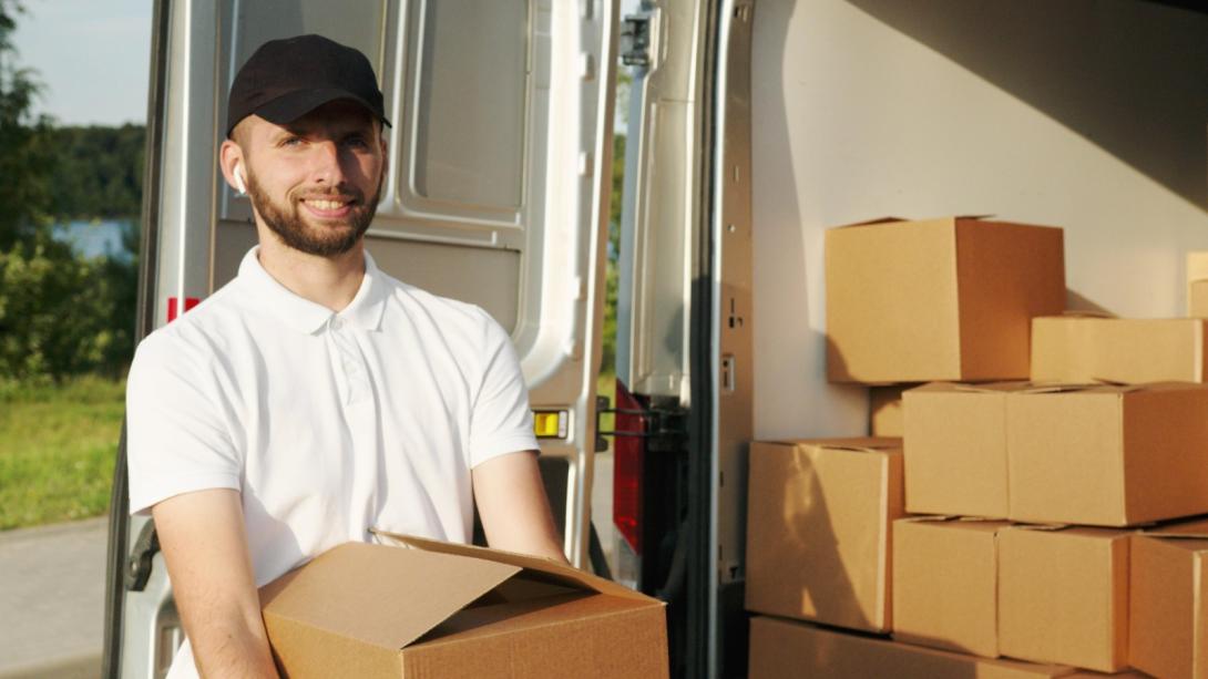 Foto de un un hombre con camiseta blanca y gorra negra alzando una caja sonriendo a la cámara