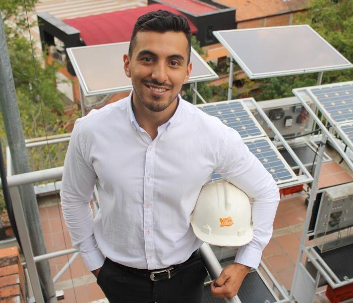 Foto de una persona con un casco posando frente a la cámara con unos paneles solares de fondo