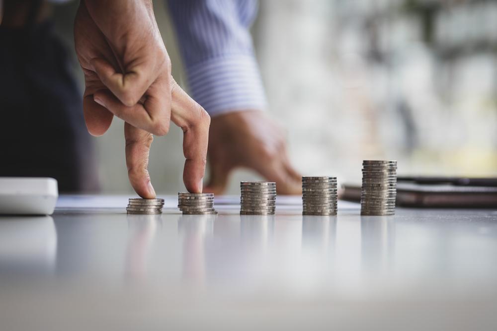 Monedas en una mesa y unos dedos pasando por ellas de forma escalonada