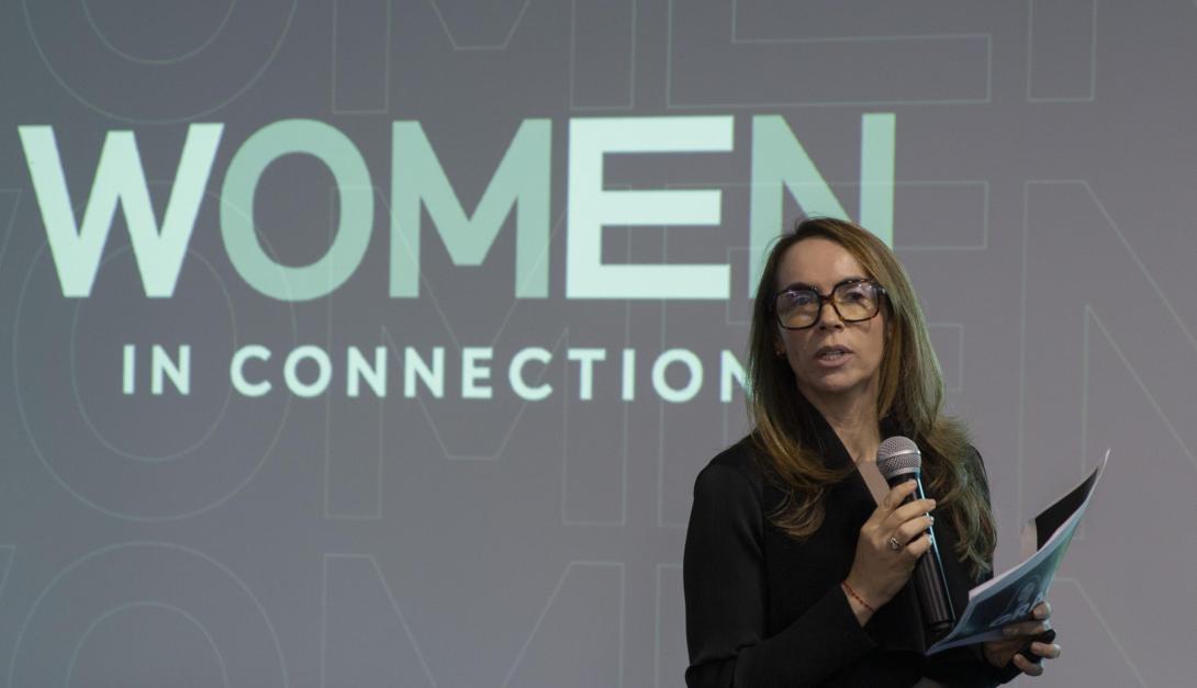 Mujer hablando en un escenario profesional con un fondo que dice Women