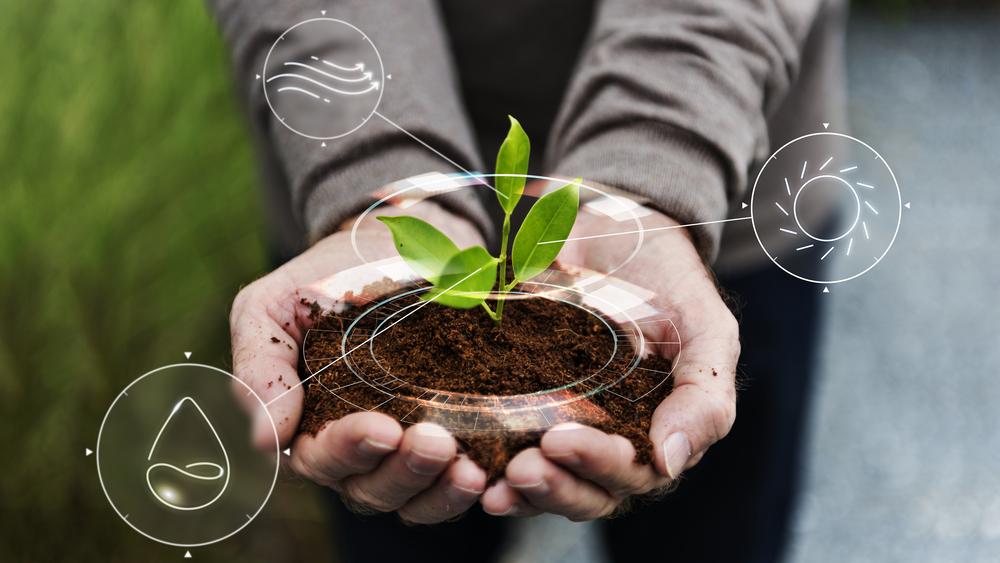 Persona sosteniendo un poco de tierra en sus manos con una planta en la parte de arriba y unos logos tecnológicos a su alrededor