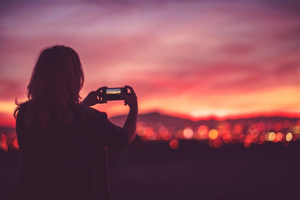 Una mujer tomando una foto sobre un cielo rosado y naranja