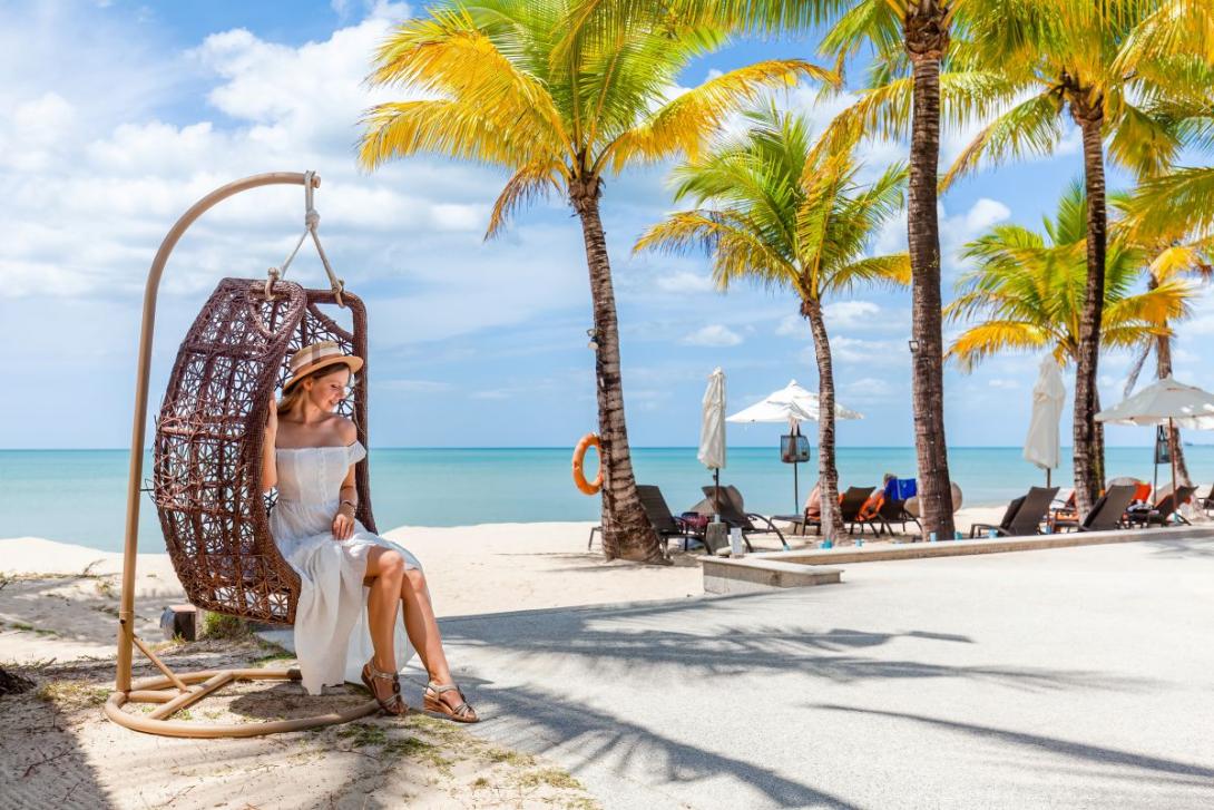 Mujer ubicada en una silla de playa con palmeras al fondo