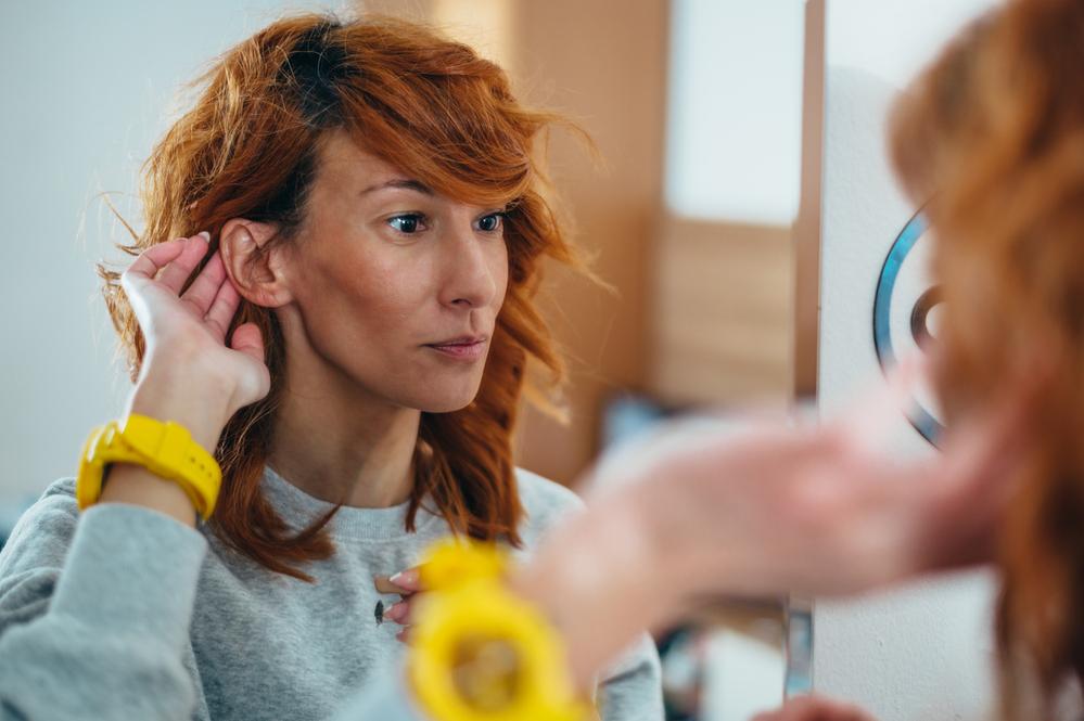 Una mujer tocandose la oreja frente al espejo