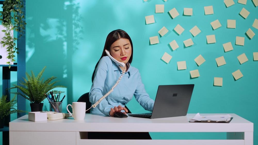 Mujer hablando por teléfono, mirando el computador y con muchos stickers pegados en la pared