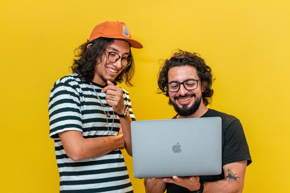 foto de dos personas mirando un pc con fondo amarillo