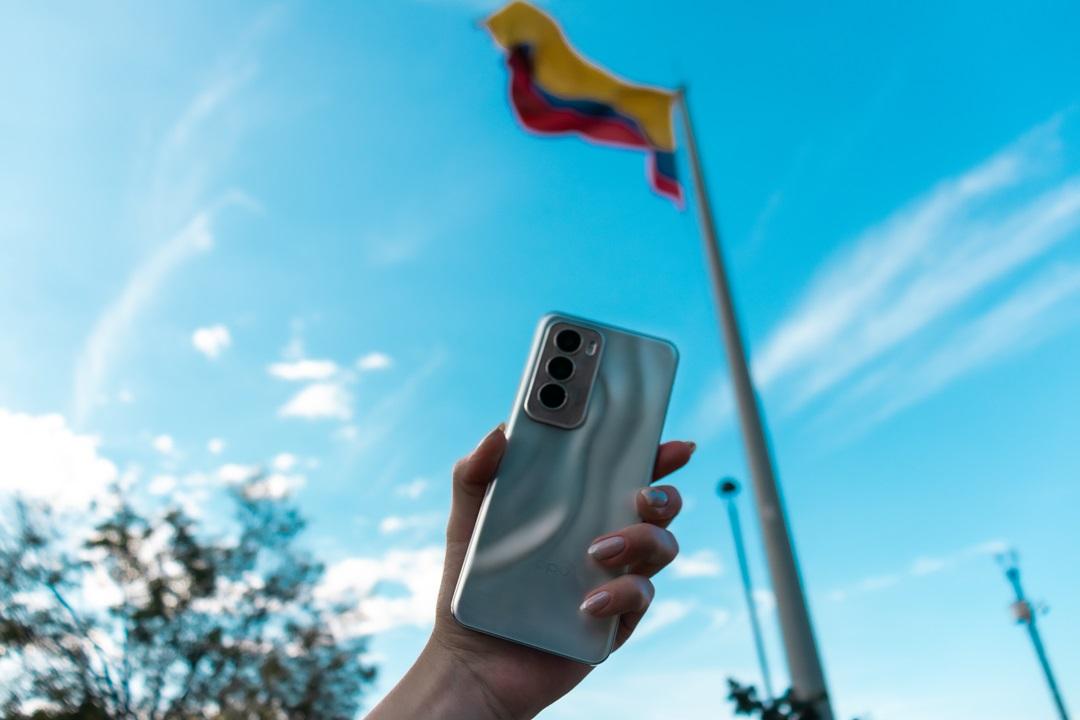 foto de una mano sosteniendo un celular con una bandera de fondo